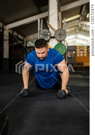 Man performing push-ups with dumbbells at gym Man performing push-ups with dumbbells at gym 138572974