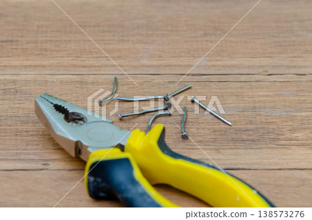 Pliers and bent nails on wooden surface showing repair process and damage Pliers and bent nails on wooden surface showing repair process and damage 138573276