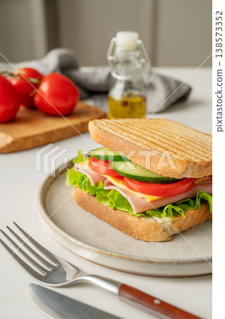 Club sandwich with ham, cheese, tomatoes, lettuce, cucumber on a plate on a white table Club sandwich with ham, cheese, tomatoes, lettuce, cucumber on a plate on a white table 138573352