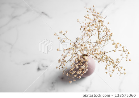 A dried bouquet of gypsophila flowers in a soft pink vase on a light marble background close up. 138573360