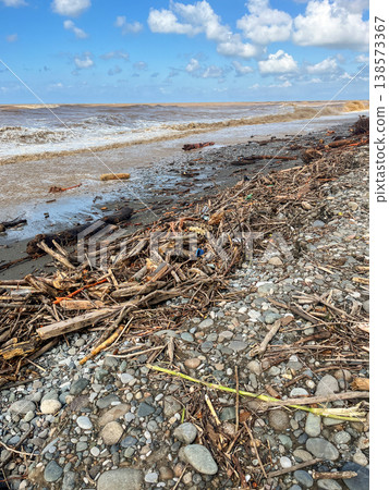 A littered pebble beach with rough waves and accumulations of debris and plastic. 138573367