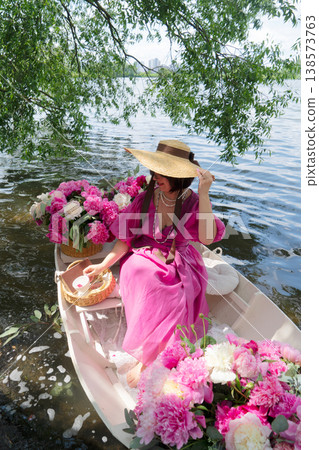 An elegant woman poses gracefully in a stunning red dress with floral arrangement against a calm water backdrop An elegant woman poses gracefully in a stunning red dress with floral arrangement against a calm water backdrop 138573763