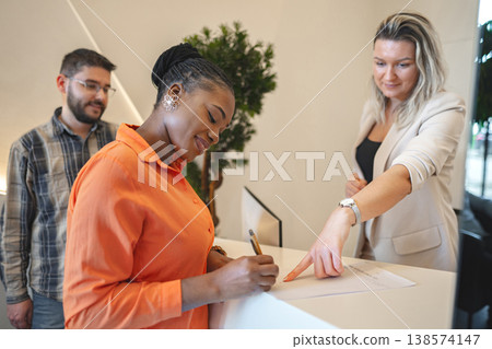 Woman Standing at Desk Signing Piece of Paper Woman Standing at Desk Signing Piece of Paper 138574147