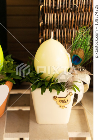 Cream egg in decorative pot with peacock feather, small wreath of boxwood, delicate ribbon and ceramic planter on rustic shelf, warm ambient light, handcrafted Easter table accent Cream egg in decorative pot with peacock feather, small wreath of boxwood, delicate ribbon and ceramic planter on rustic shelf, warm ambient light, handcrafted Easter table accent 138574228