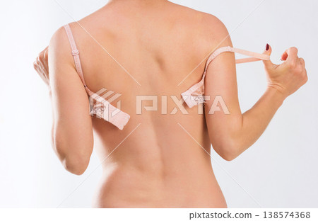 Figure of woman in peachy lingerie taking off her bra, standing in her underpants, backshot 138574368