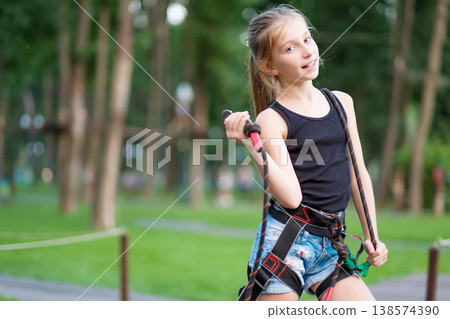 Cute teenage girl in safety harness on her belt in rope park Cute teenage girl in safety harness on her belt in rope park 138574390