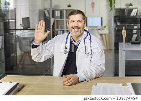 Smiling doctor greeting patient on online telemedicine video call in modern clinic Smiling doctor greeting patient on online telemedicine video call in modern clinic 138574454