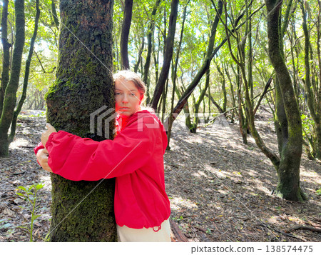 Person in red jacket caring outdoors. Enthusiastic volunteer with open arms in woodland setting. Dedicated individual in vibrant coat showing kindness amid sunlit forest trail 138574475