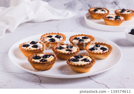 Baked mini tartlets with cottage cheese and black currant on a plate on the table 138574611