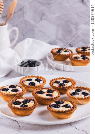 Baked mini tartlets with cottage cheese and black currant on a plate on the table vertical view 138574614