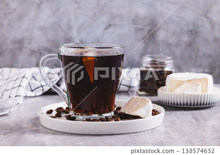 Black coffee with a piece of brie cheese in a glass on the table Black coffee with a piece of brie cheese in a glass on the table 138574632