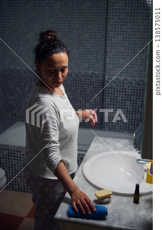 Middle-Aged Woman in Pyjamas Performing Morning Skincare Routine at Bathroom Sink Middle-Aged Woman in Pyjamas Performing Morning Skincare Routine at Bathroom Sink 138575011