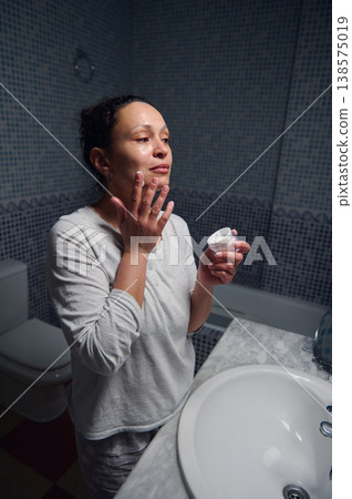 Middle Aged Woman in Pyjamas Applying Face Cream During Morning Skincare Routine Middle Aged Woman in Pyjamas Applying Face Cream During Morning Skincare Routine 138575019