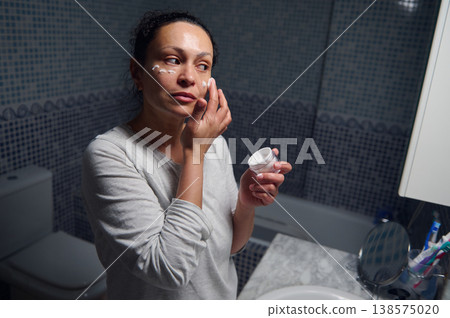 Middle-Aged Woman Applying Face Cream During Morning Beauty Routine in Pajamas Middle-Aged Woman Applying Face Cream During Morning Beauty Routine in Pajamas 138575020