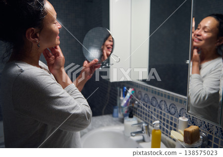 Middle-Aged Woman in Pajamas Doing Morning Skincare Routine in Bathroom Mirror Middle-Aged Woman in Pajamas Doing Morning Skincare Routine in Bathroom Mirror 138575023