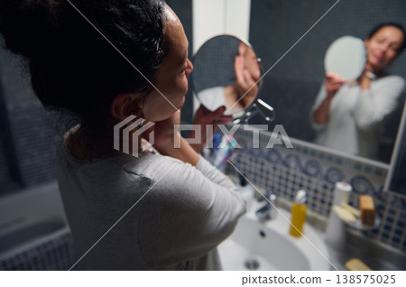 Middle Aged Woman in Pajamas Caring for Her Face During Morning Skincare Routine at Bathroom Mirror Middle Aged Woman in Pajamas Caring for Her Face During Morning Skincare Routine at Bathroom Mirror 138575025