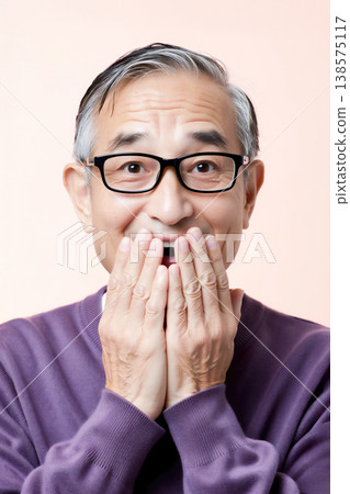 A senior man smiles and covers his mouth with both hands. 138575117