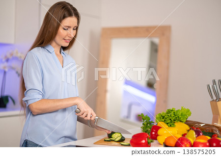 Contented young woman cutting vegetables and looking busy Contented young woman cutting vegetables and looking busy 138575205