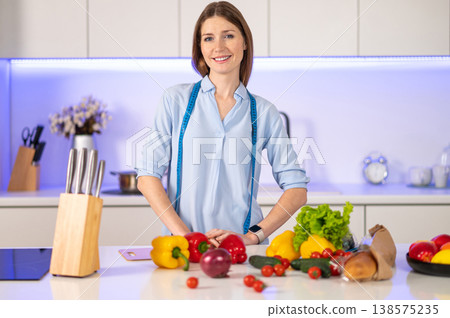 Smiling young woman near the table full of vegetables in the kitchen 138575235