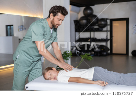 Physiotherapist guiding girl during back recovery training Physiotherapist guiding girl during back recovery training 138575727