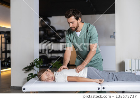 Physiotherapist performing manual back massage for child Physiotherapist performing manual back massage for child 138575737