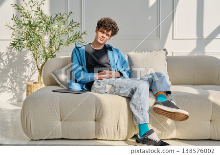 Portrait of handsome young man with curly hair sitting on sofa Portrait of handsome young man with curly hair sitting on sofa 138576002