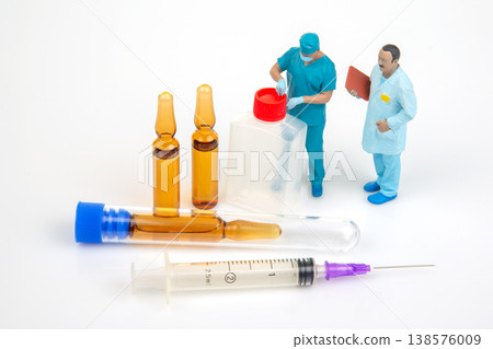 Miniature people stand near medical supplies in a lab setting as one draws liquid from vials Miniature people stand near medical supplies in a lab setting as one draws liquid from vials 138576009