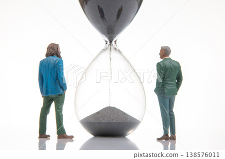 Miniature figurines of two people standing next to an hourglass with black sand  138576011