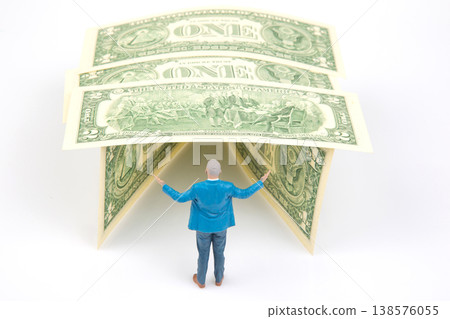 Miniature people stand under dollar bills as a roof while posing with hands open in a creatively  138576055