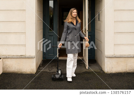Mother exiting apartment holding scooter and lunch bag for children at school 138576157