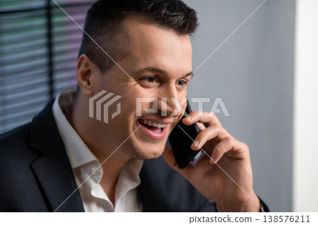 Businessman in suit laughing during phone call while posing in office Businessman in suit laughing during phone call while posing in office 138576211