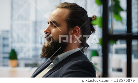 CEO leans back in his office chair engaging in a guided meditation session with white noise, using a meditation app. Commitment to mindfulness for career success and mental clarity. Camera B. 138576879