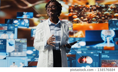 Cheerful woman showing futuristic medical visuals on digital videowall during conference. Jolly African american doctor presenting medical research data and 3D anatomy models dashboards, camera A Cheerful woman showing futuristic medical visuals on digital videowall during conference. Jolly African american doctor presenting medical research data and 3D anatomy models dashboards, camera A 138576884
