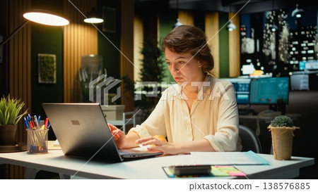 Stressed employee works late and uncontrollably eating a snack, feeling hungry and overeating due to a mental health condition. Stress eating disorder creates an unhealthy lifestyle. Camera A. 138576885