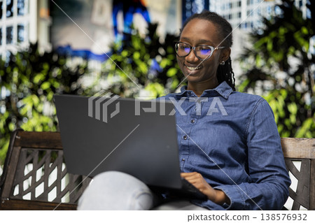 Happy student on park bench holding laptop pleased after receiving excellent grade on online assignment. Cheerful young girl outside satisfied by high exam marks seen on notebook 138576932