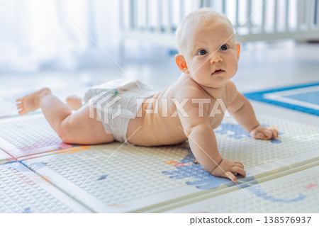 Baby lying on play mat learning to crawl and get on all fours. Infant practicing motor skills and development at home. Early childhood growth, milestones and active learning concept 138576937