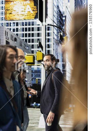 Professional businessman checking his smartphone apps on crowded street, walking along busy avenue with a big crowd of multiethnic pedestrians. Adult on his morning commute downtown. Professional businessman checking his smartphone apps on crowded street, walking along busy avenue with a big crowd of multiethnic pedestrians. Adult on his morning commute downtown. 138576960