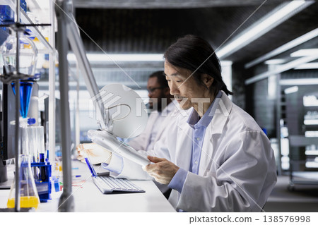 Chemist uses laboratory lamp to examine liquid in test tube for clarity and color changes. Lab technician holds test tube to light source for reaction monitoring and impurity detection Chemist uses laboratory lamp to examine liquid in test tube for clarity and color changes. Lab technician holds test tube to light source for reaction monitoring and impurity detection 138576998