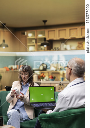 Chroma key screen laptop held by old male physician during in-home routine checkup, does health exam for senior woman. Doctor conducting assisted living and preventive treatment. Chroma key screen laptop held by old male physician during in-home routine checkup, does health exam for senior woman. Doctor conducting assisted living and preventive treatment. 138577000