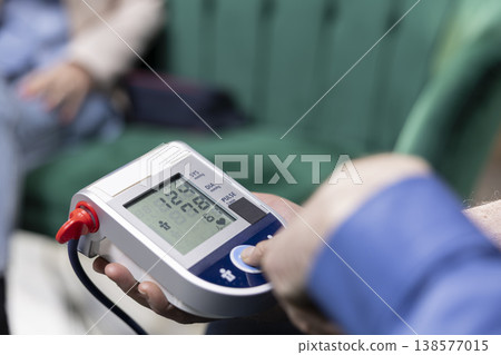 Close up of person pressing button to start measuring blood pressure, checking vital signs and pulse pressure for disease prevention and safety. BP monitor used to ensure wellness at home. 138577015