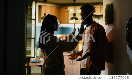 Black furious man and woman arguing in a dark hallway at home, facing relationship difficulties and domestic dispute. Young couple looking frustrated and upset, aggressive argument. Black furious man and woman arguing in a dark hallway at home, facing relationship difficulties and domestic dispute. Young couple looking frustrated and upset, aggressive argument. 138577038