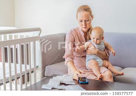 Mother sitting on sofa holding baby while calculating monthly expenses with receipts at home. Stressed mom managing budget and childcare. Financial stress, parenthood and real life concept 138577577