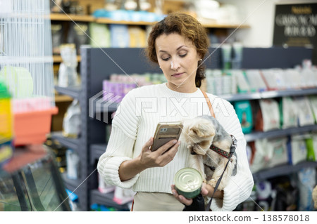 Woman client with Yorkshire terrier photographs nutrition packaging scans QR code 138578018