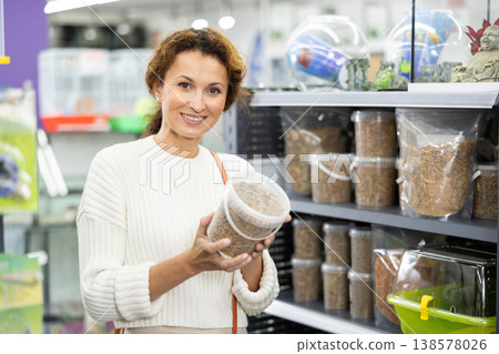 Female shopper selecting dry pelleted food for turtles in pet store 138578026