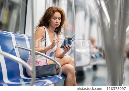 Adult woman sitting in subway car with phone Adult woman sitting in subway car with phone 138578097