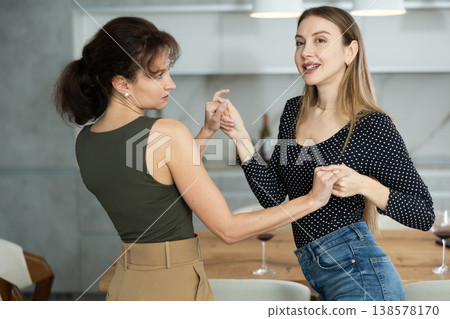 Two joyful middle-aged women dancing together at the kitchen-table with wineglasses 138578170