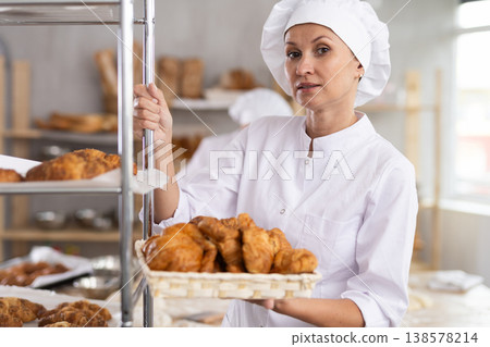 Portrait of old female baker working in bakehouse, holding tray with fresh bakery goods on kitchen 138578214