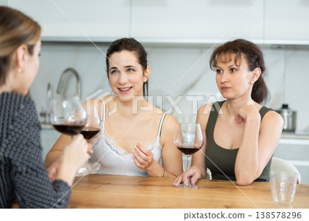 Three happy middle-aged women sitting at table with a glass of wine while having lively conversation 138578296