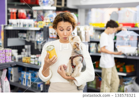Woman with curious Yorkshire terrier choosing canned dog food in pet store Woman with curious Yorkshire terrier choosing canned dog food in pet store 138578321