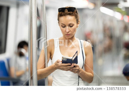 Adult woman standing in subway car with phone Adult woman standing in subway car with phone 138578333